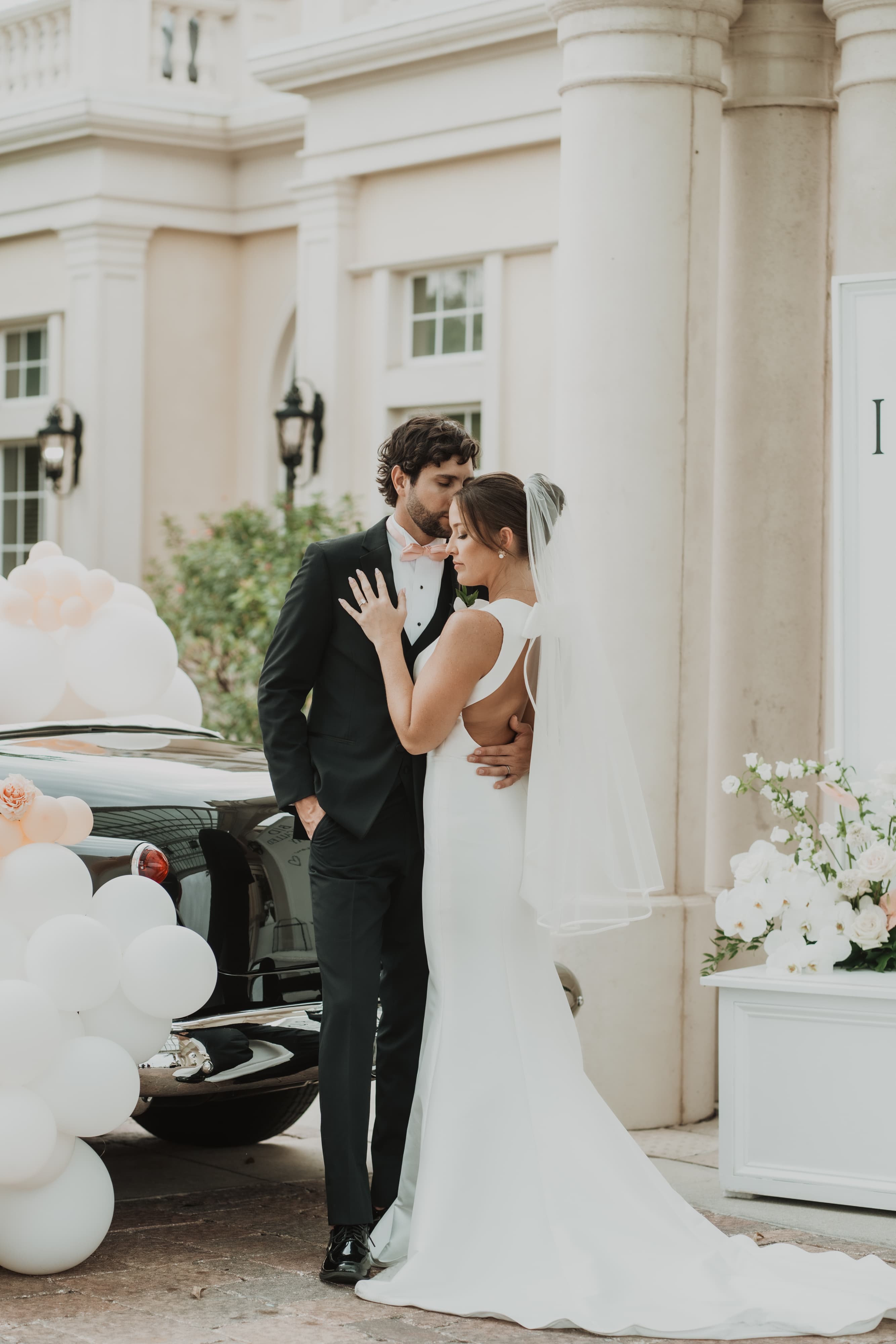 Bride and groom embracing beside a vintage car outside their wedding venue